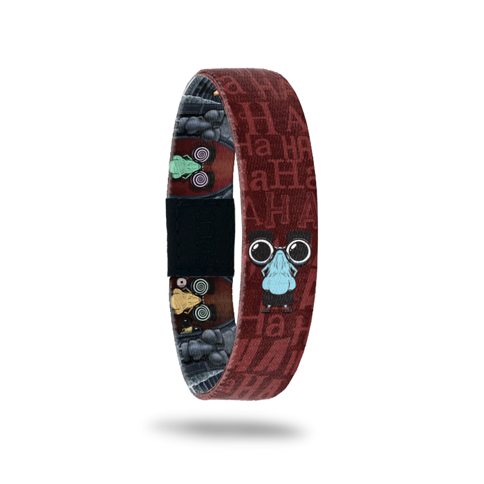Brown and dark reddish bracelet with "HA HA" all around the design. Comes with a pin of a goofy big nose with mustache and glasses. Inside is the same goofy monster with glasses adn swirly eyes.