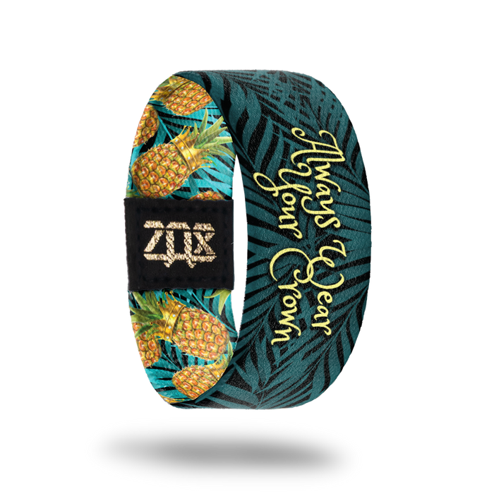 Inside of elastic wristband that says Always Wear your Crown in a light yellow font. Dark blue/green plants are in the background