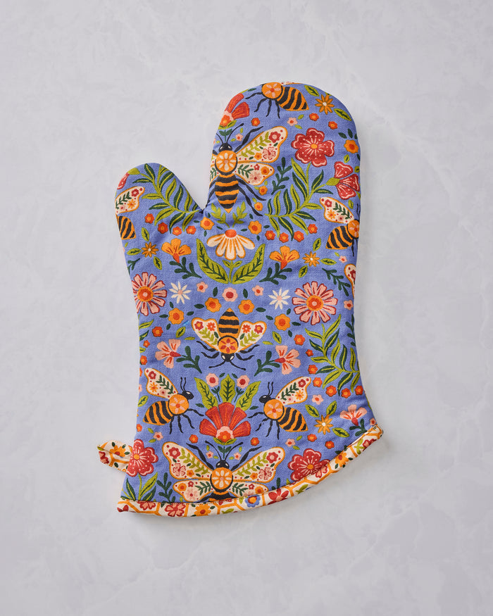 Reverse-side view of a blue floral oven mitt with bee, butterfly, flower, and leaf print.