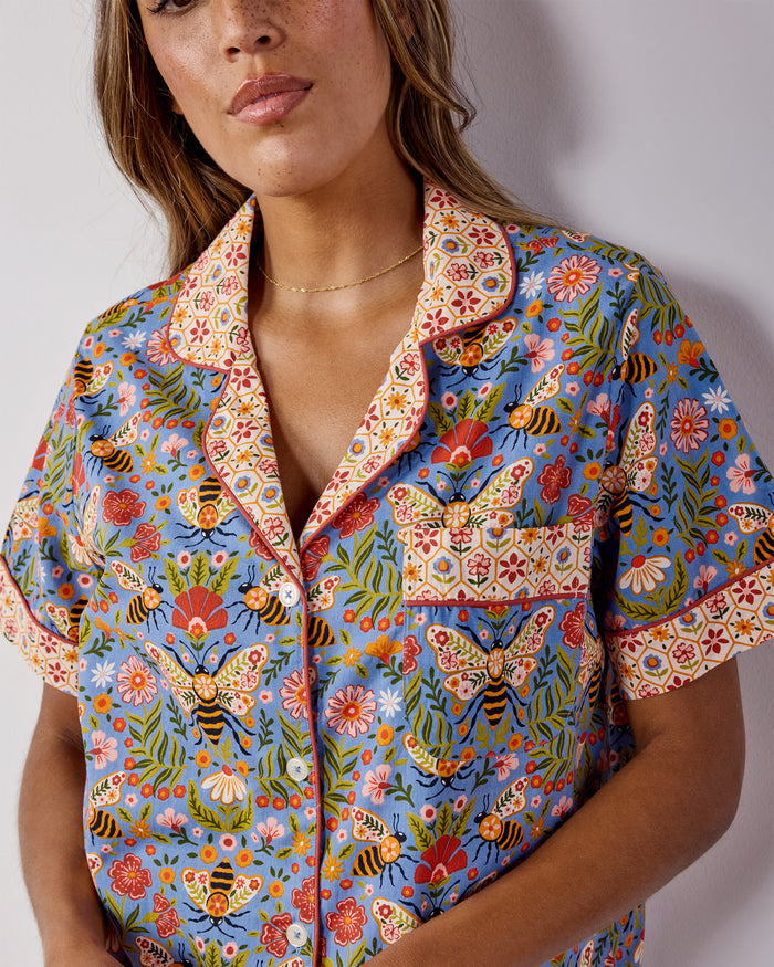 Close-up of the Bee Tapestry pajama top showing its notched collar, button front, chest pocket, and blue floral-and-bee print.