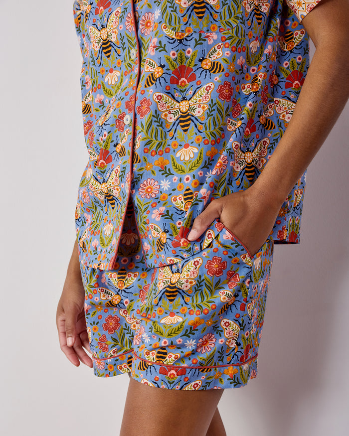 Close-up of the Bee Tapestry pajama shorts showing the elastic waistband, side pocket, contrasting trim, and blue floral-and-bee print.