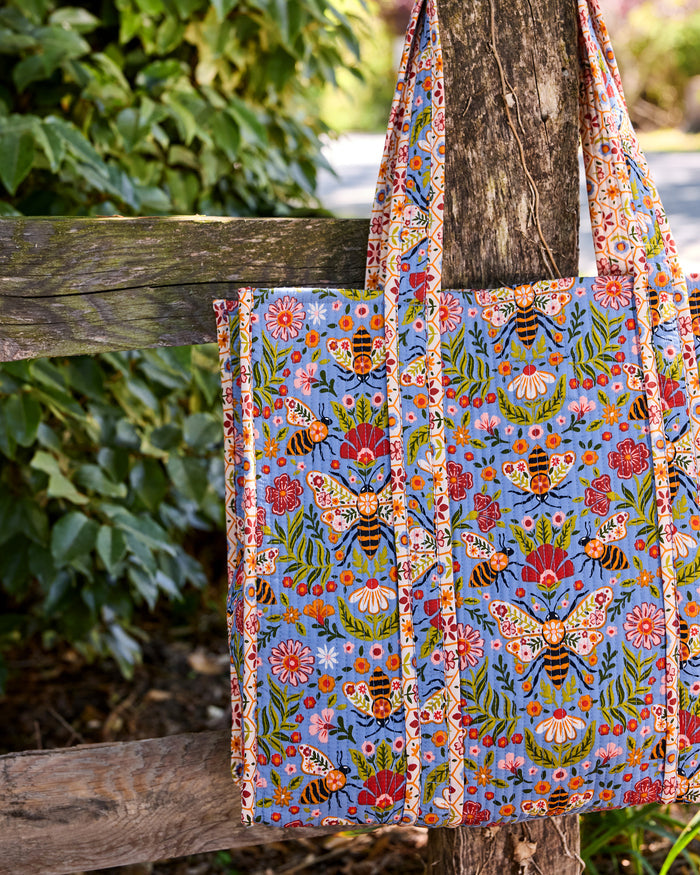 Close-up of the Bee Tapestry traveler tote showing its blue bee-and-floral print, handles, and side construction.