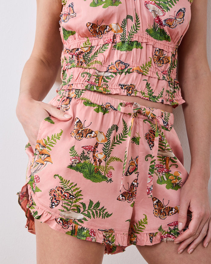 Close-up of the rosewood Butterfly Forager short pajama set, showing the ruffle-trimmed tank, elastic waistband, pockets, and butterfly, mushroom, and fern print.