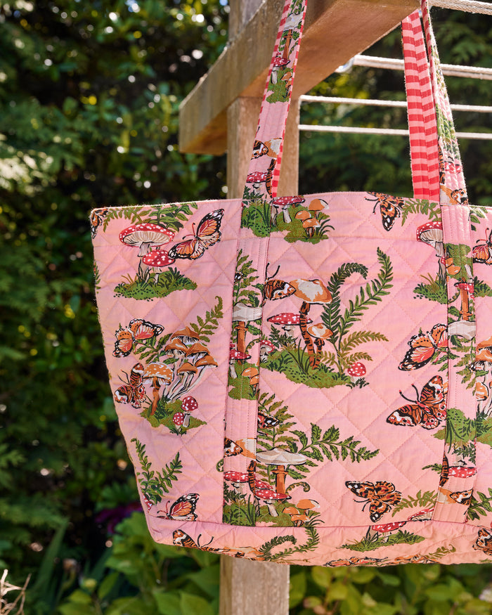 Close-up of the rosewood quilted weekend bag showing its butterfly, mushroom, and fern print, straps, and attached pouch.