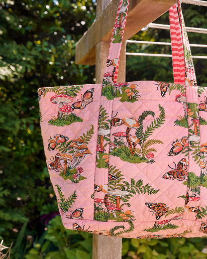 Close-up of the rosewood quilted weekend bag showing its butterfly, mushroom, and fern print, straps, and attached pouch.