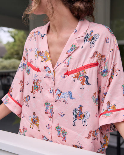 Close-up of the cropped pink pajama top with a horse-and-cowgirl print, red trim, notched collar, and front buttons.
