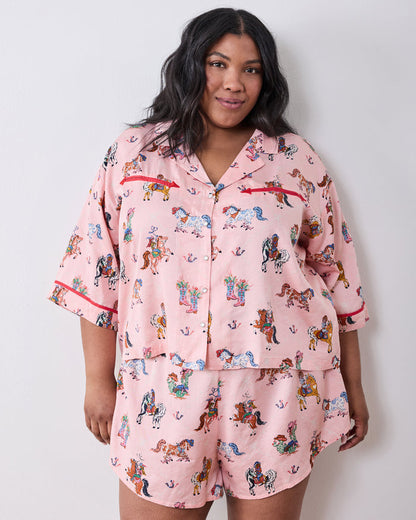 Model wearing the pink short pajama set with a horse-and-cowgirl print, collared button-front top, and matching shorts.