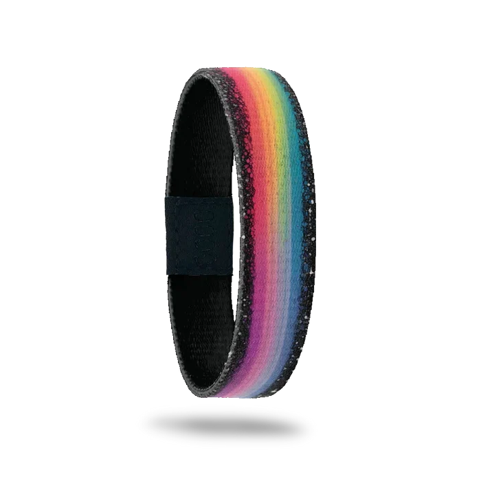 Wristband single is a blured rainbow the entire length of the band and has black and white specs on both edges. The inside is sold black and reads It All Works Out Better Than You Ever Expected.