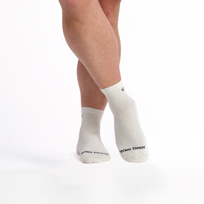 Models feet crossed wearing the men's 9014 solid lightweight quarter sock on white featuring the charcoal logo on toe