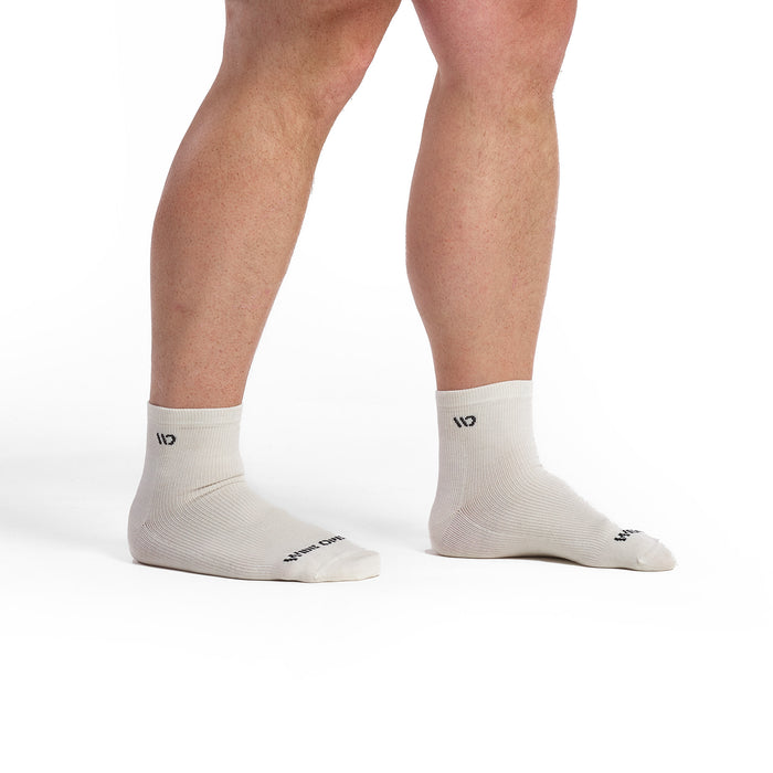 Models feet facing to the right wearing the 9014 solid lightweight quarter sock in white featuring all white body and charcoal logo