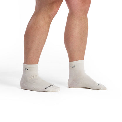 Models feet facing to the right wearing the 9014 solid lightweight quarter sock in white featuring all white body and charcoal logo