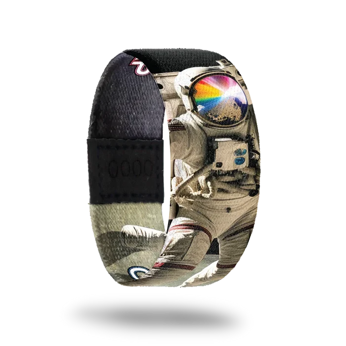 Wristband strap with a black base. A realistic black and white photo of an astronaut jumping on the moon. His face shield is reflecting off a rock and rays of rainbow colors. The inside is the same and reads One Giant Leap.